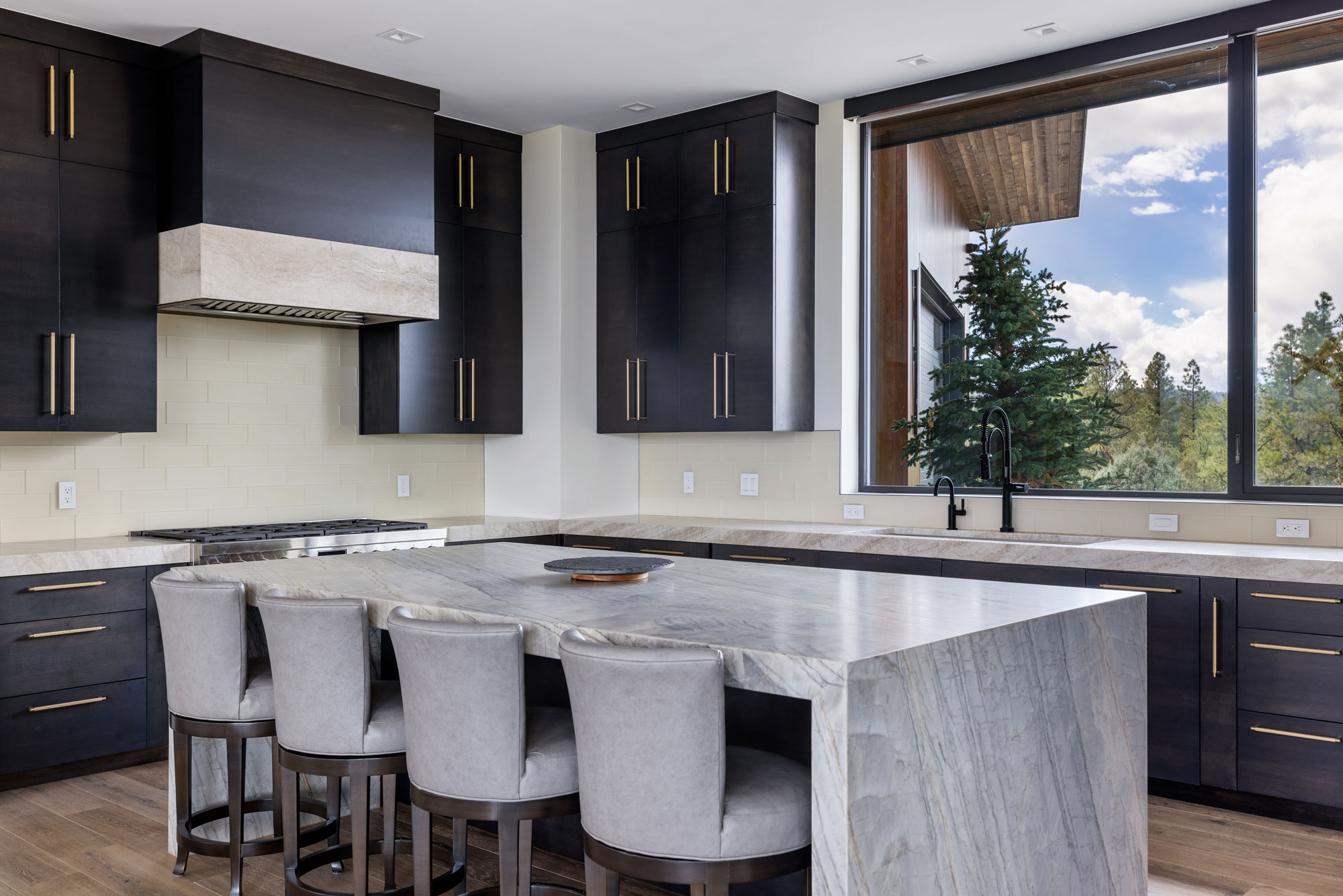 Modern kitchen with dark cabinetry, large window, and marble island.