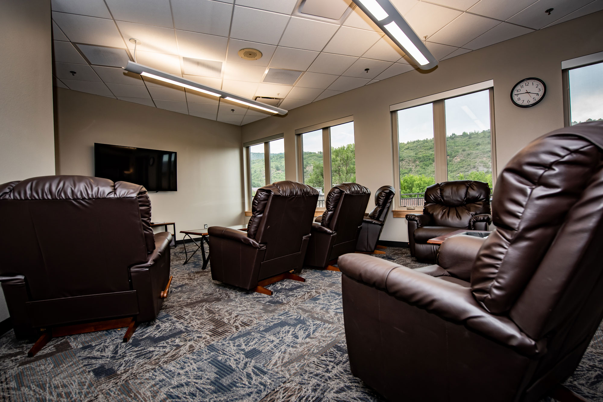 Leather office chairs in a comfortable lounge area with large windows and a wall-mounted TV.