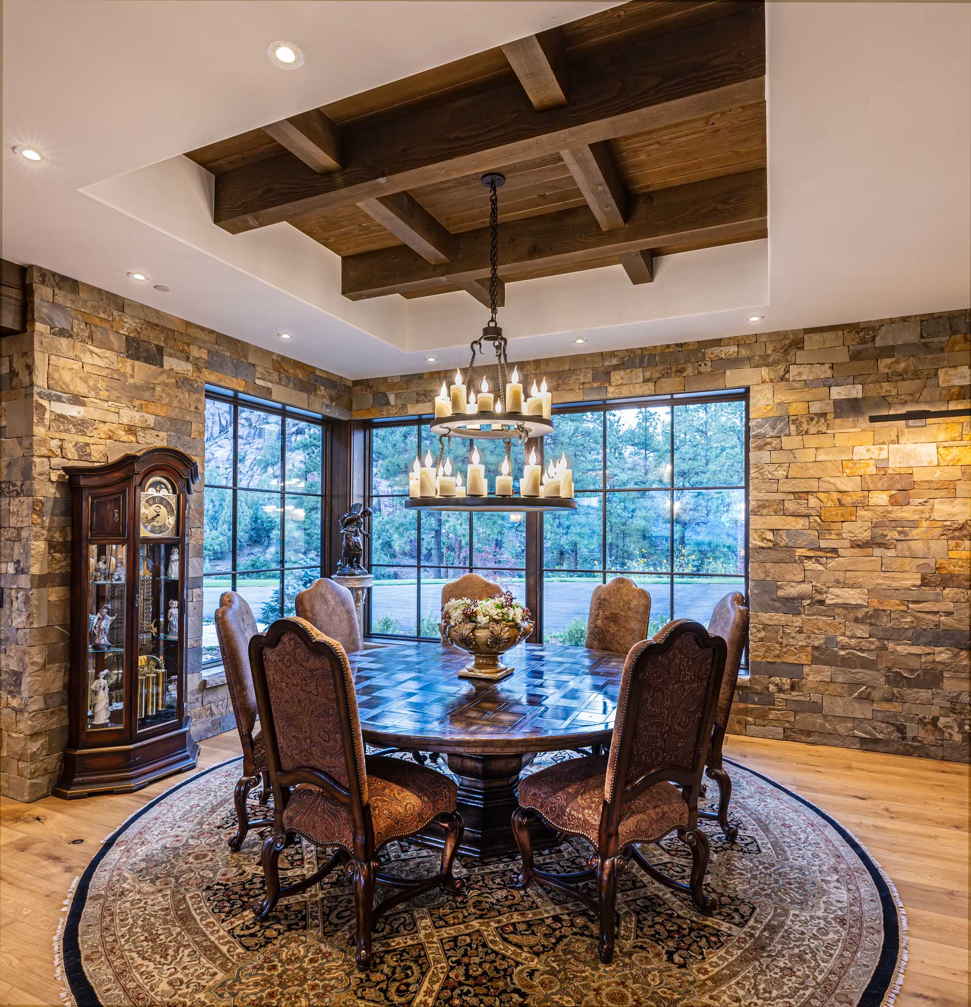 Elegant mountain estate dining room with rustic stone walls and wooden ceiling beams.