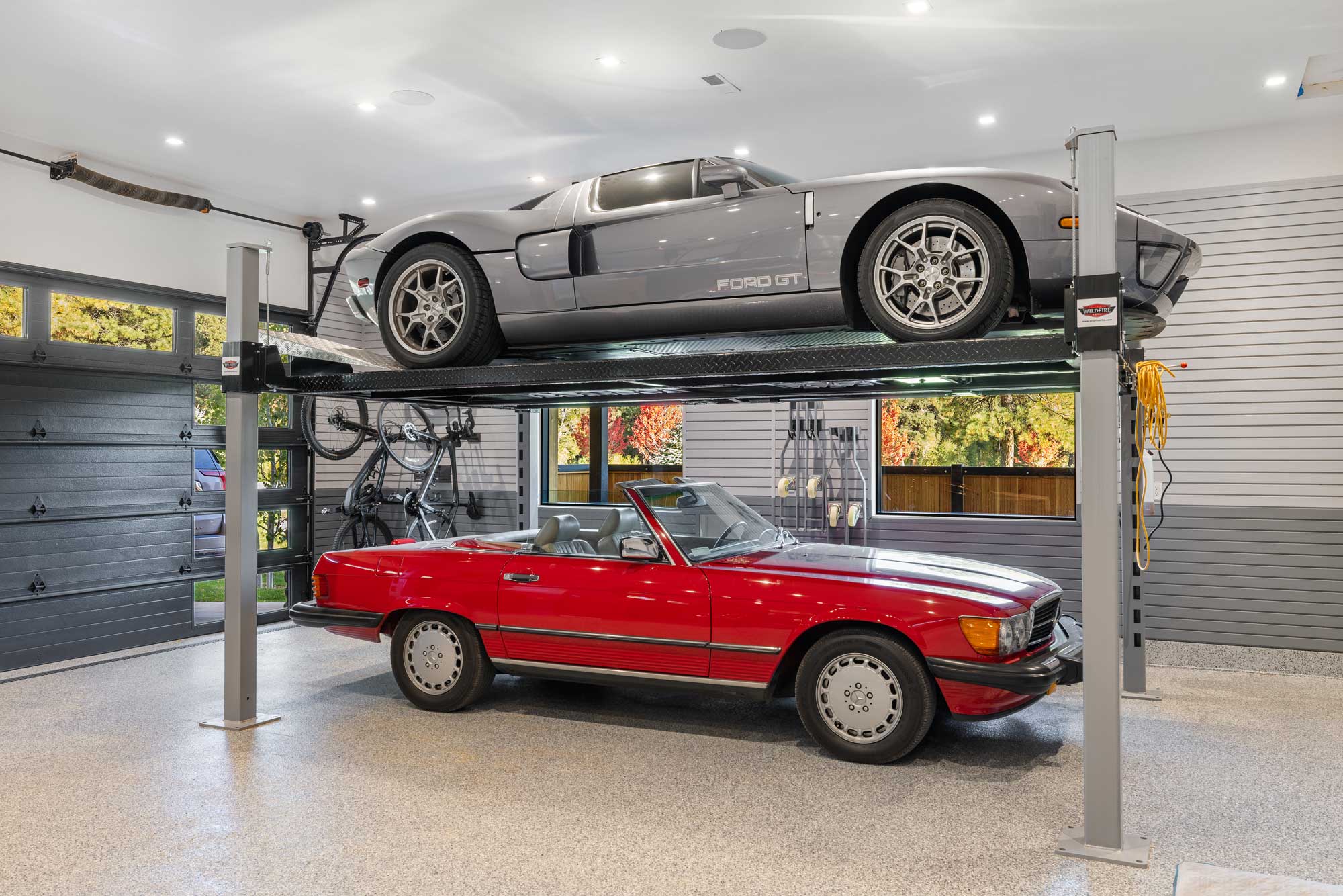 Luxury car storage with a sleek silver Ford GT on a hydraulic lift and a classic red convertible bel.