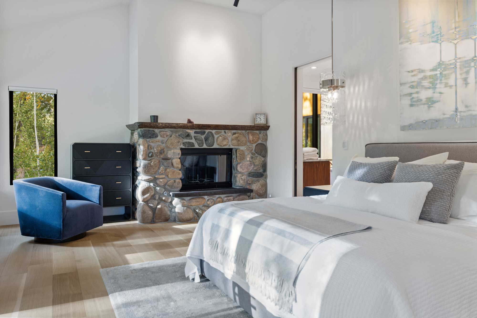 Interior view of a modern bedroom with a stone fireplace, white walls, and contemporary furniture.