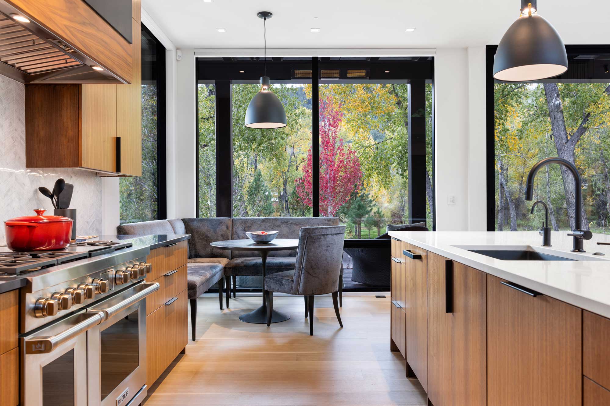 Modern kitchen featuring large windows overlooking colorful trees, with wooden cabinets and sleek ap.