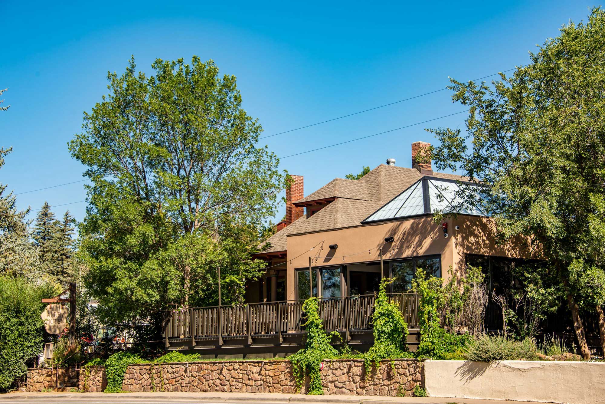 House with lush greenery and a wooden deck under a clear blue sky.