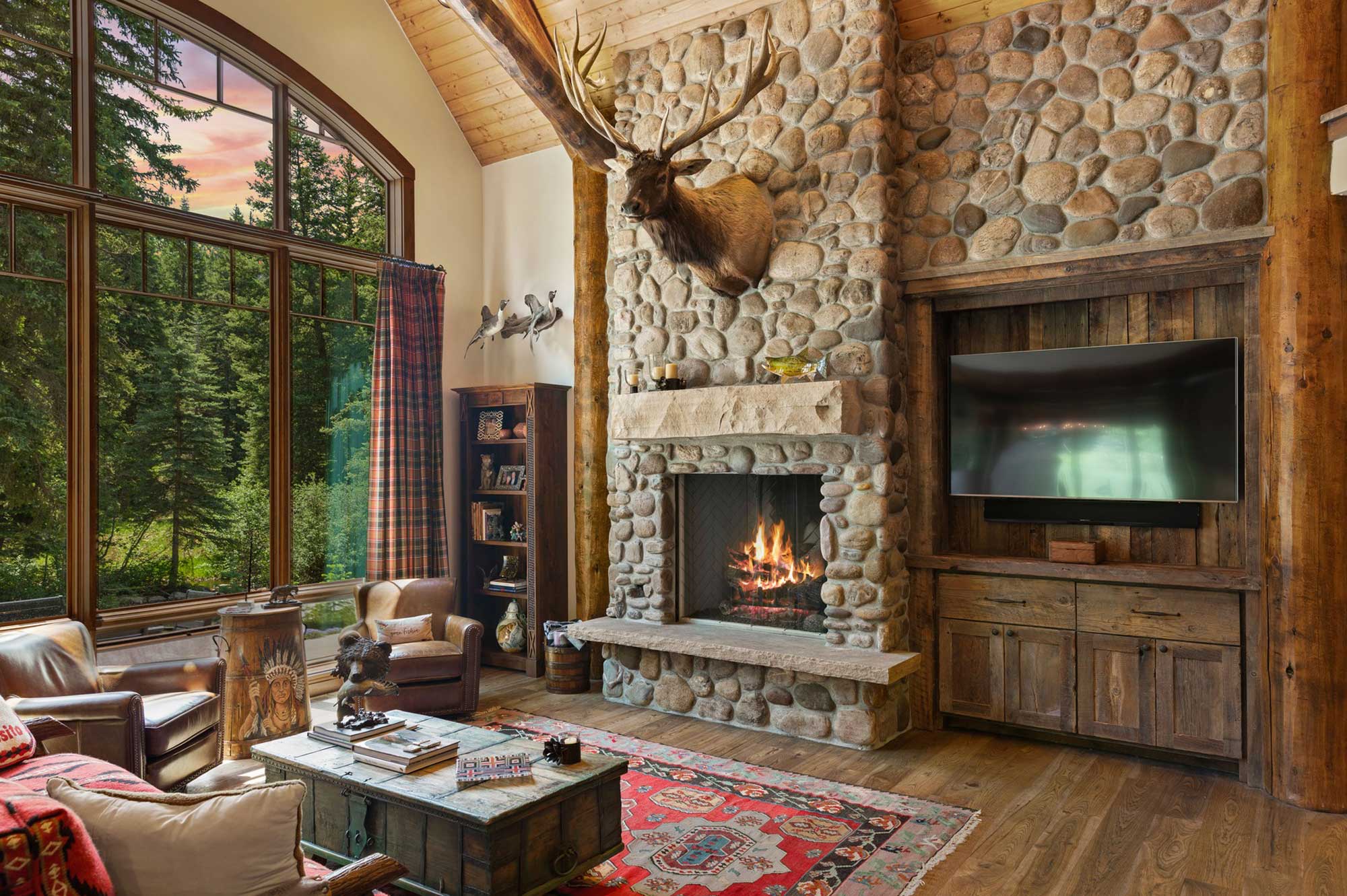 Cozy living room with stone fireplace and large windows overlooking nature.
