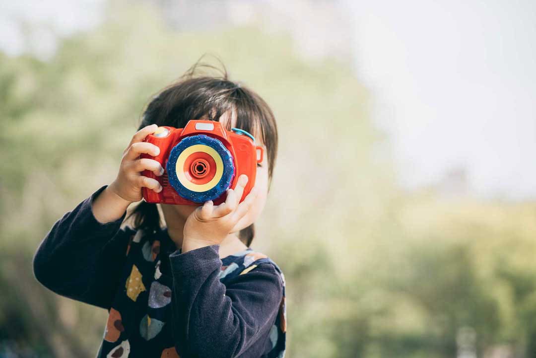 Child holding a toy camera, symbolising snapshot, focus and new perspectives in business growth.