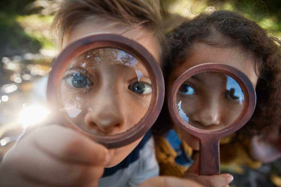 Children looking through magnifying glasses, symbolising financial clarity and focus provided by Redcurrant Services.