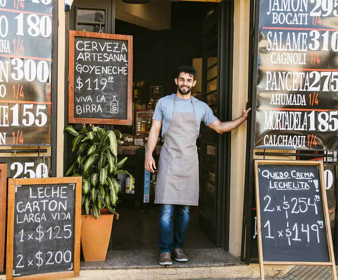 Independent shop owner standing proudly at the entrance, representing SME entrepreneurs.