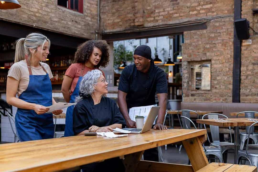 Restaurant team gathered around a laptop discussing business finances and planning.