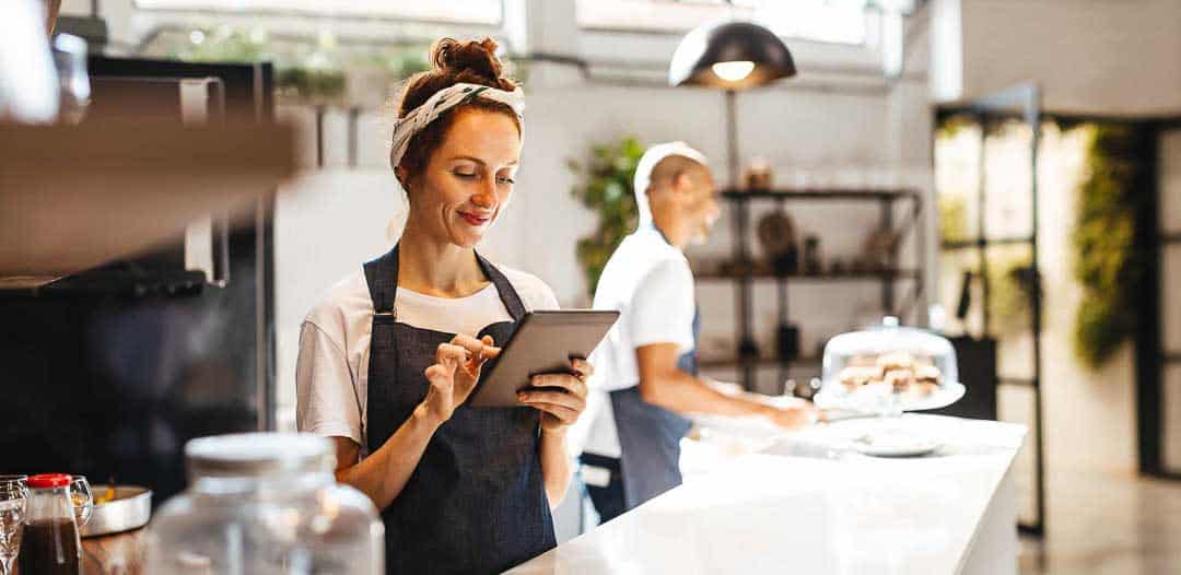 Café owner using a tablet for business planning inside a modern coffee shop.