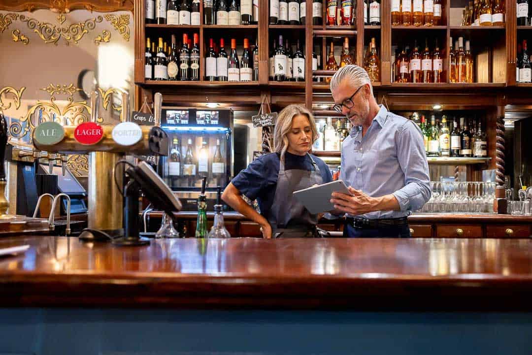 Pub owners reviewing finances together on a tablet behind the bar in London.