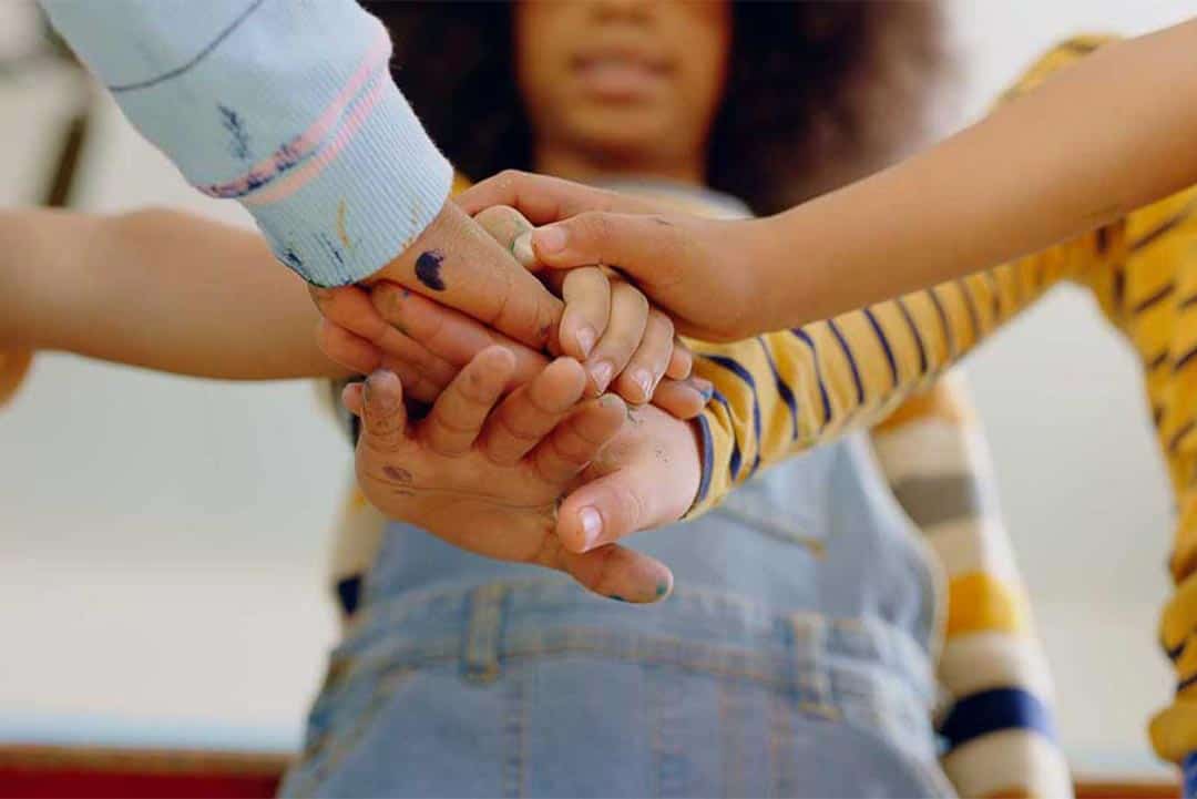 Close-up of teamwork with children’s hands stacked together, symbolising collaboration and SME support.