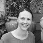 Relaxed smiling woman outdoors in garden with large ceramic pot and green foliage.