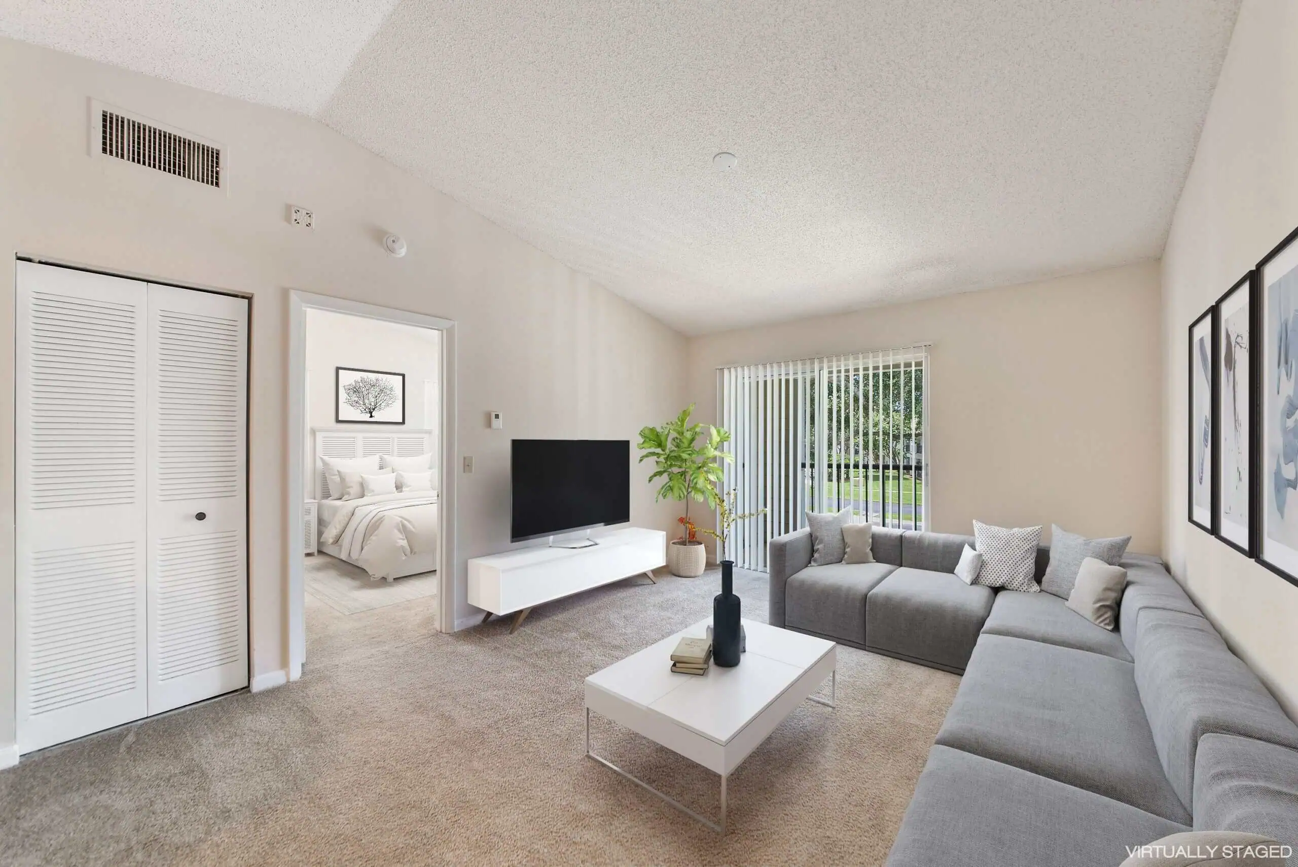Living room with grey sectional sofa and flat screen tv. Sliding glass door to outdoor patio. There is also a view into the bedroom.