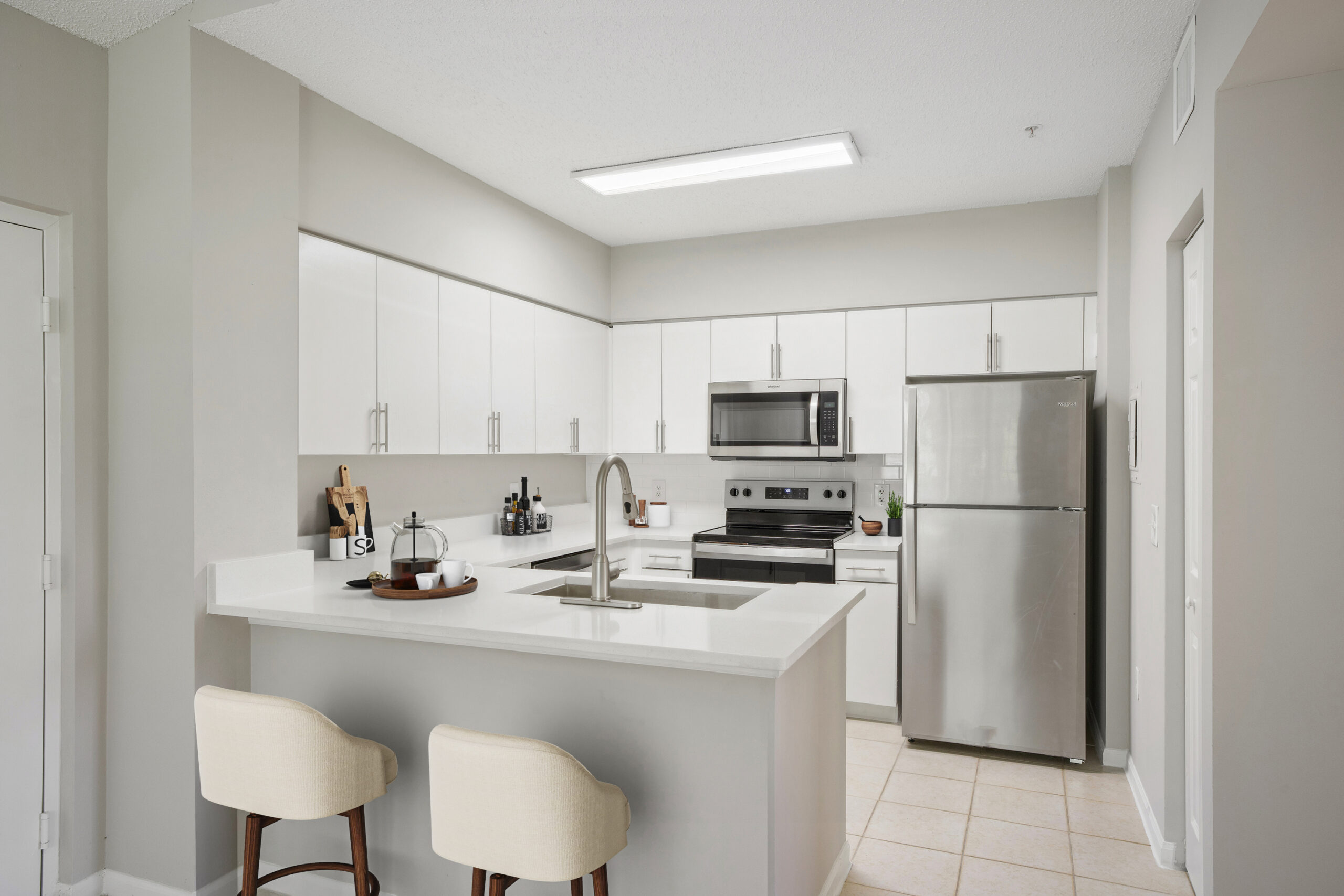 A kitchen with a refrigerator, microwave, and bar stools.
