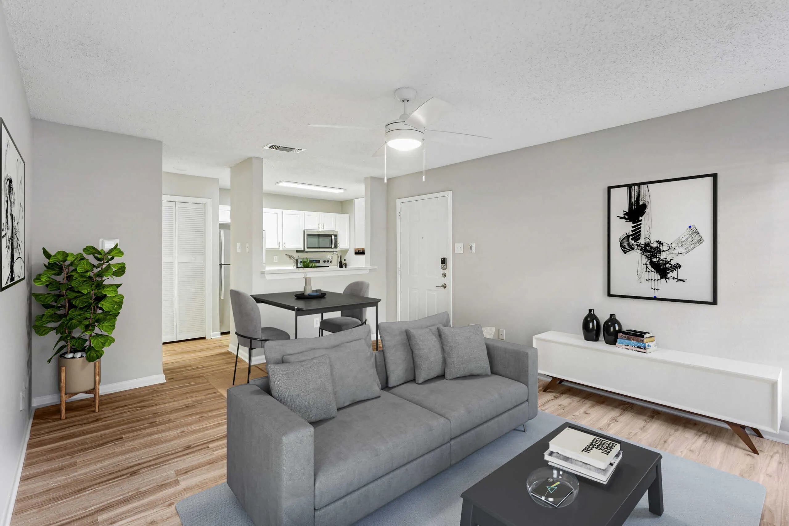 A modern living room with a grey sofa, open kitchen, wood-style floors, and simple decor.