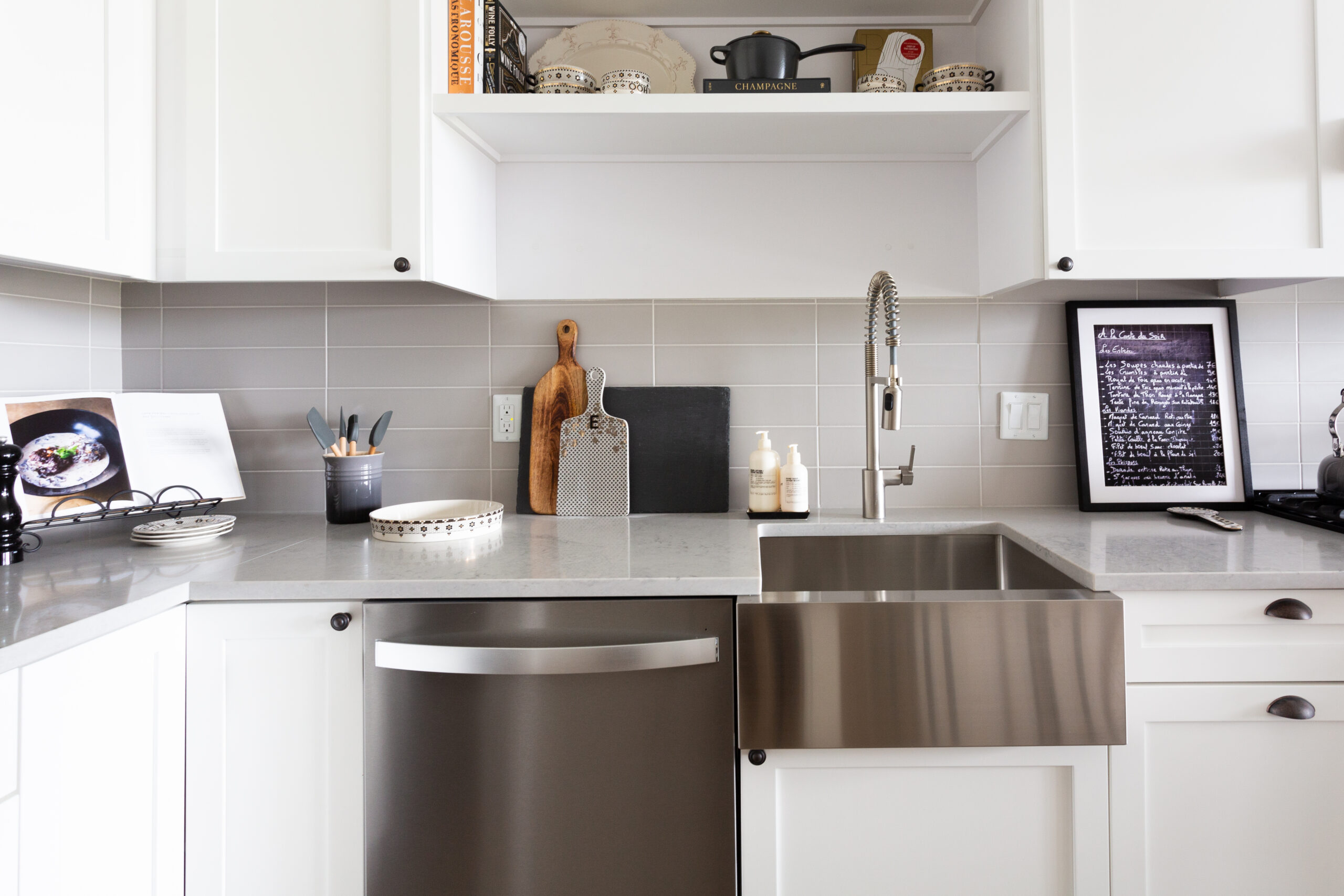 modern apartment kitchen with stainless steel dishwasher, gray countertops and white cabinets