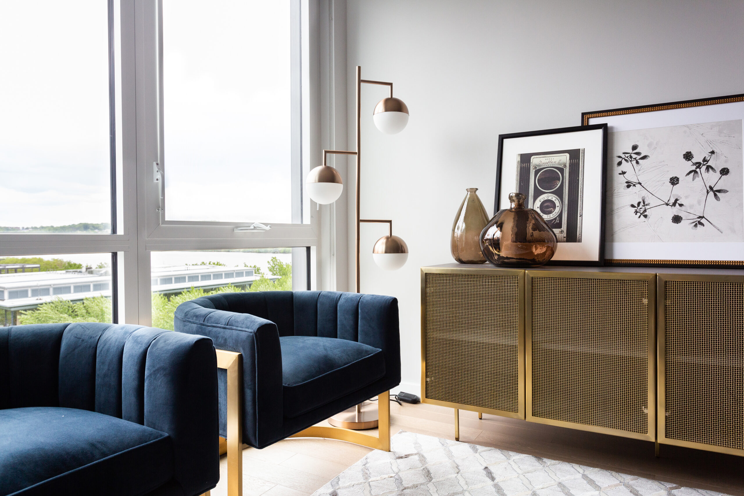 modern apartment living room with two blue chairs, floor lamp, buffet, and large windows