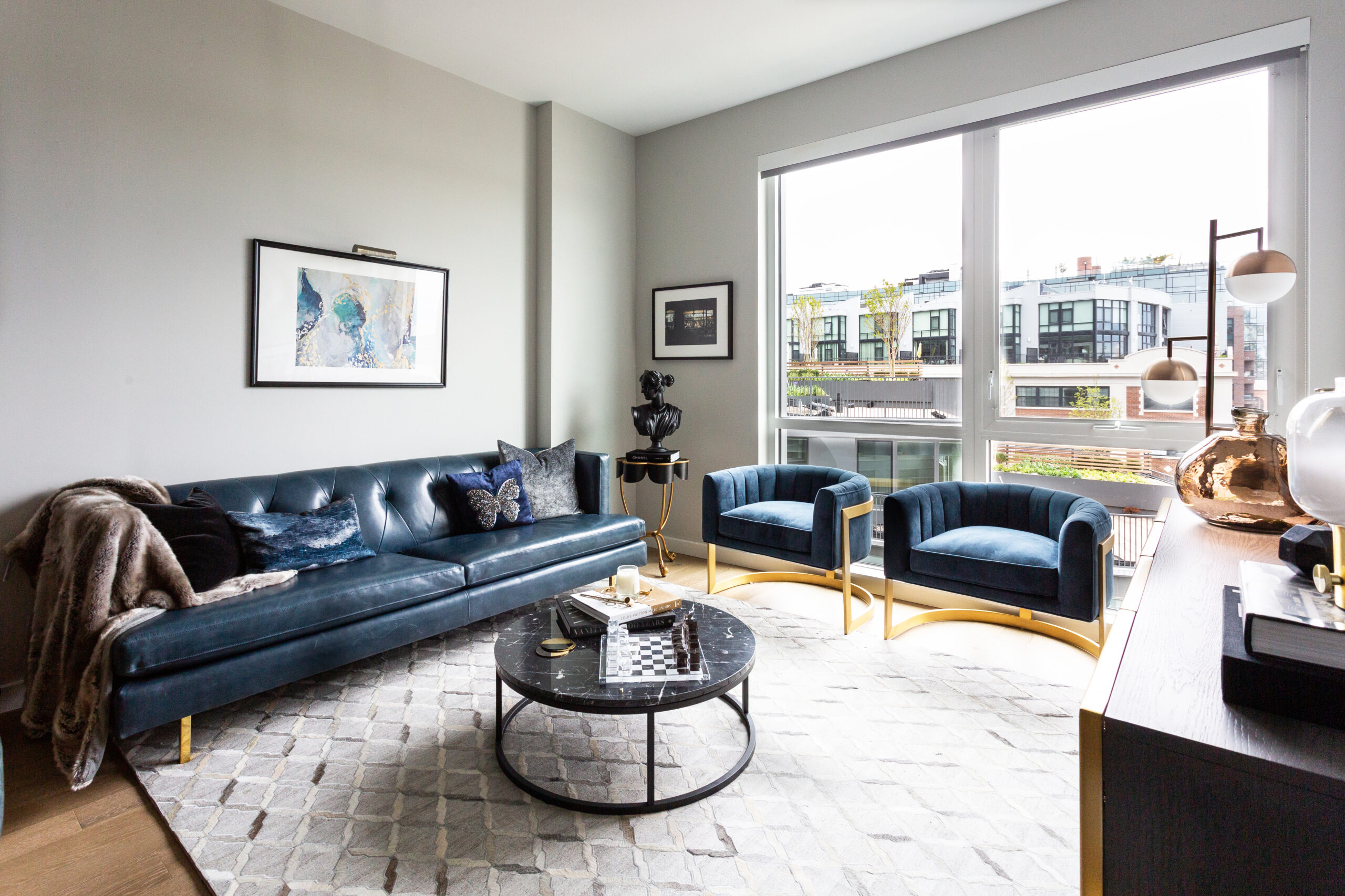 modern apartment living room with blue leather sofa, round marble coffee table, blue chairs and large windows