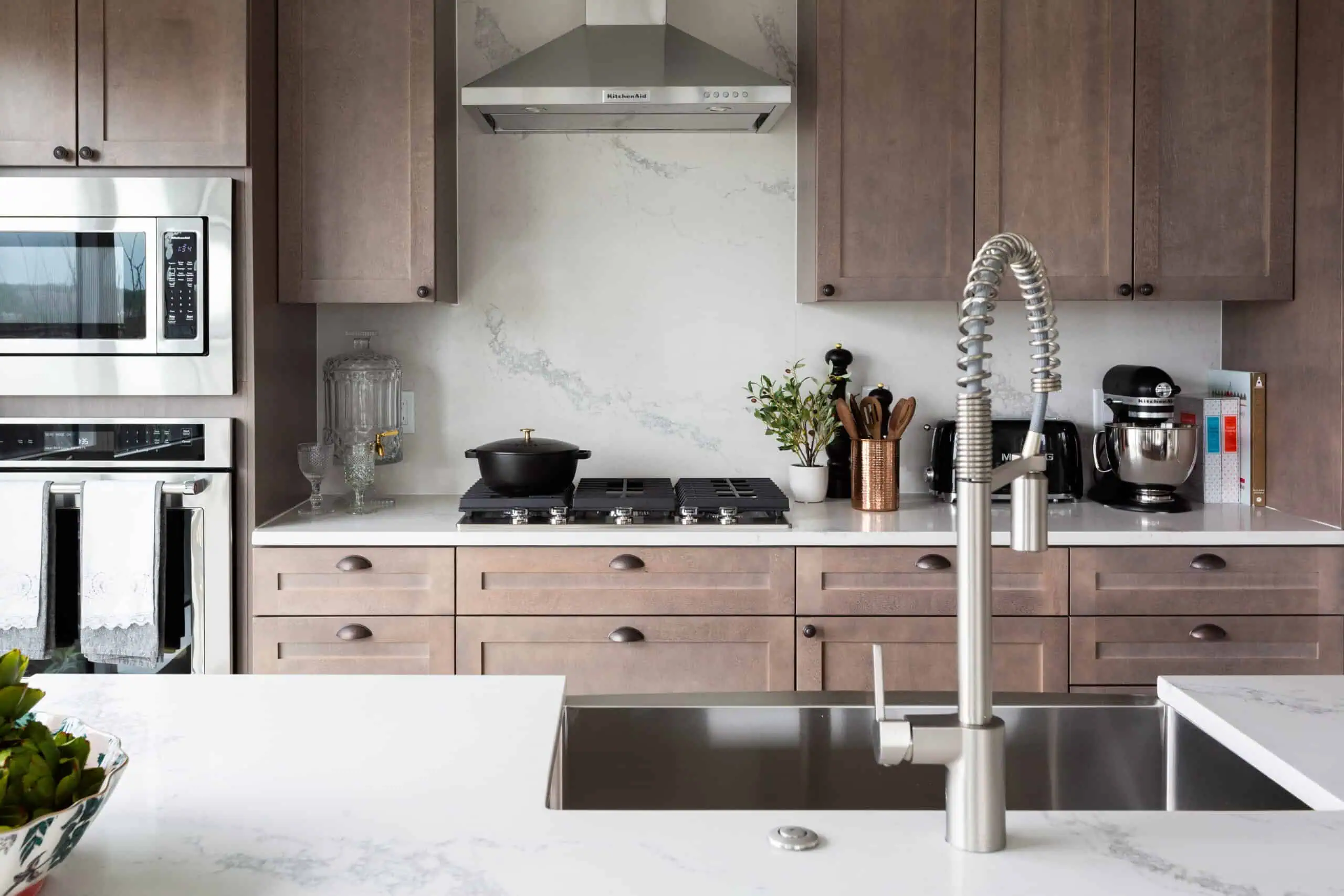 modern apartment kitchen with stainless steel apliances, marble backsplash and light brown cabinets