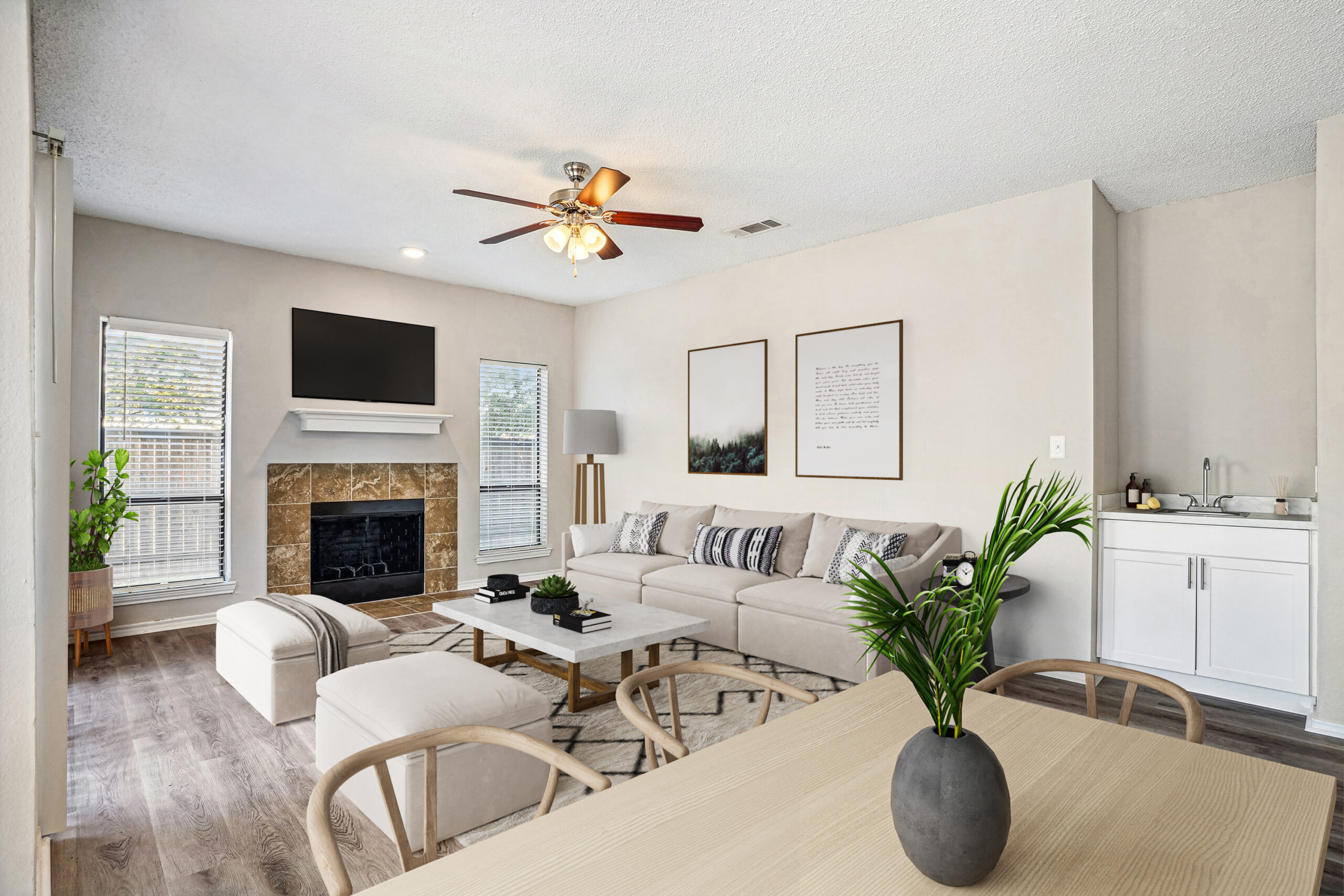 Living room with wood dining room table, couch, mounted tv, paintings, and ceiling fan.