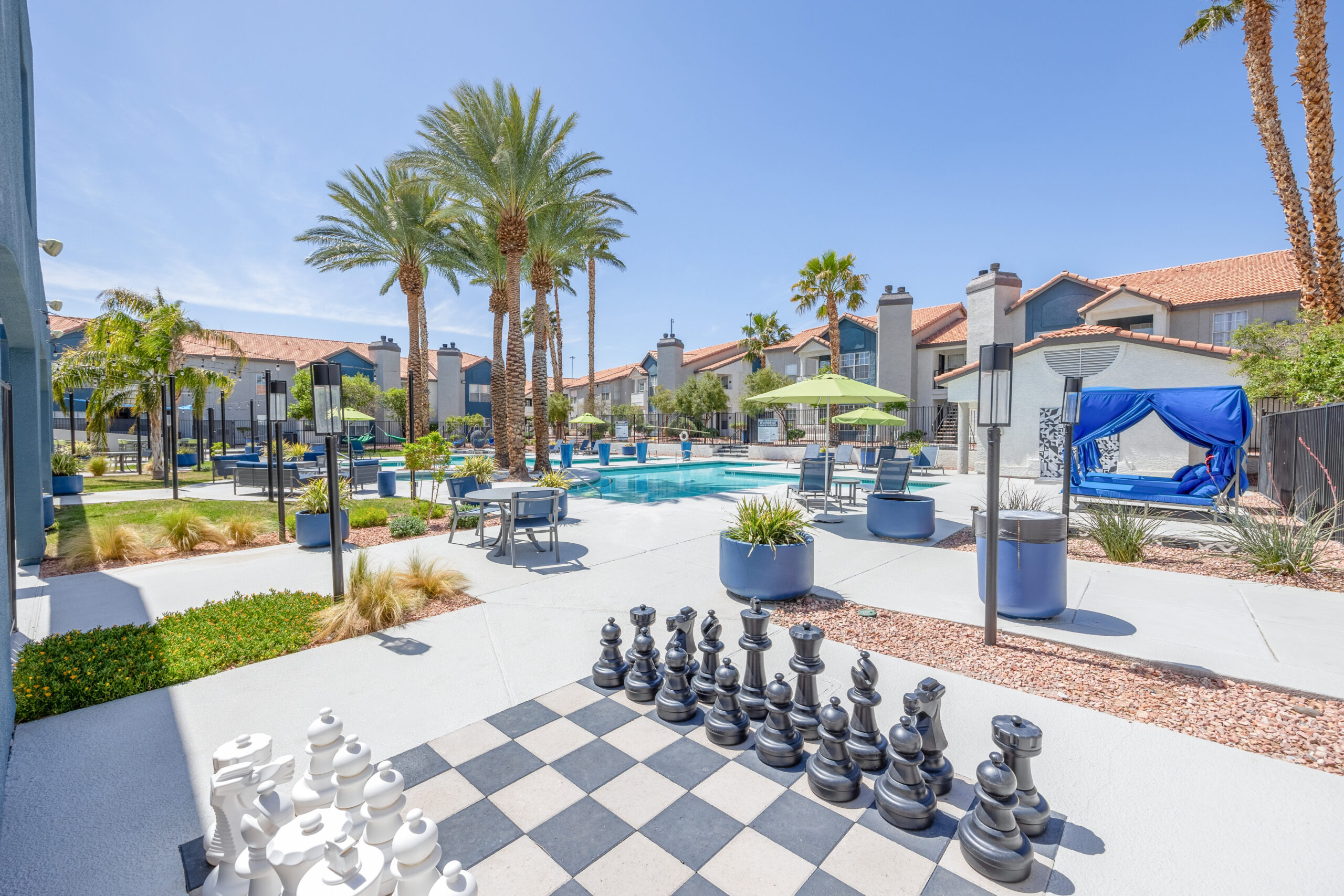 Outdoor pool courtyard with large Chess board, lounge chairs and cabanas by the pool and nicely landscaped with palm trees.