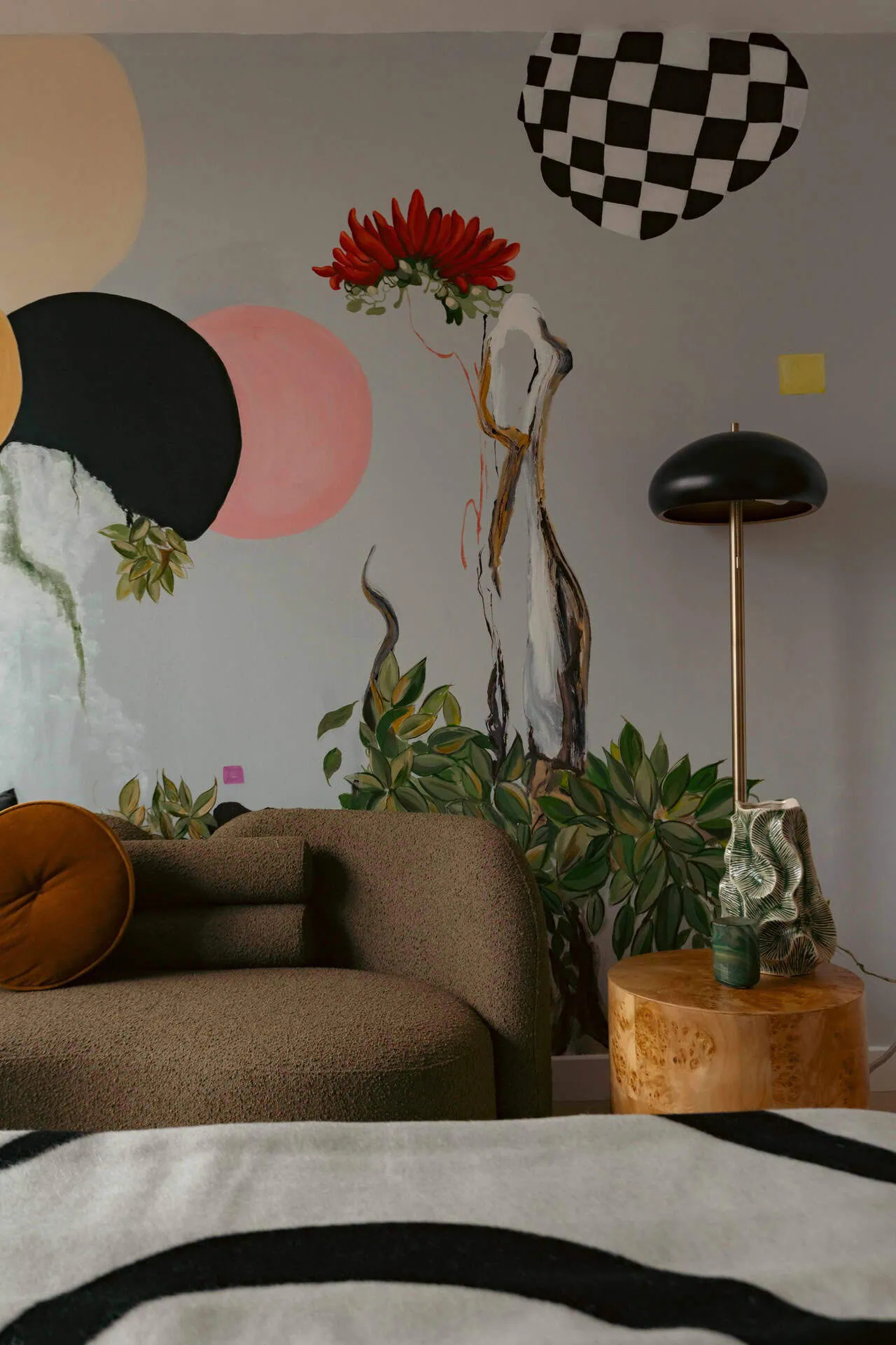 A living room with a couch, a lamp and a wall mural.