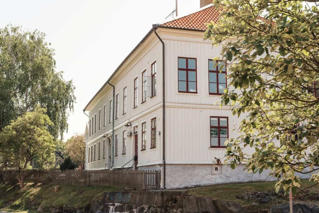 Långsträckt vit träbyggnad i två våningar med röda fönster och tegeltak, placerad ovanför en klippa i Klippan, Göteborg.