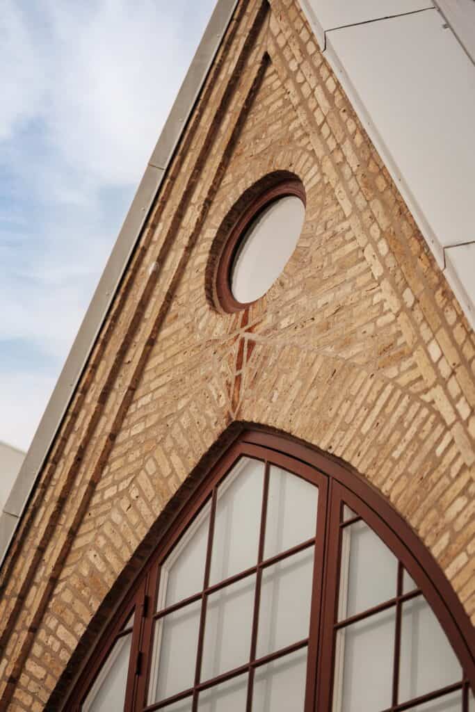 Vägg av tegel med stort fönster och rund fönsteröppning, modern arkitektur.