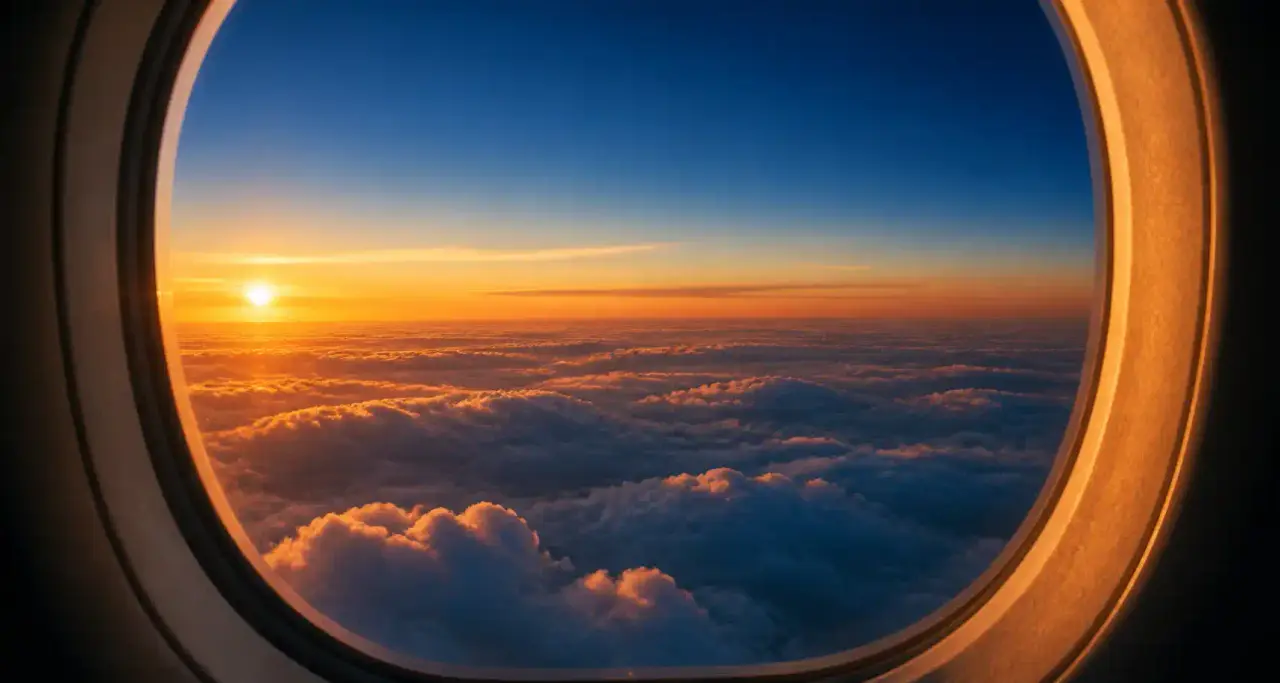 Vue depuis le hublot d'un avion sur une mer de nuages au coucher du soleil, ciel bleu azur et horizon ambré
