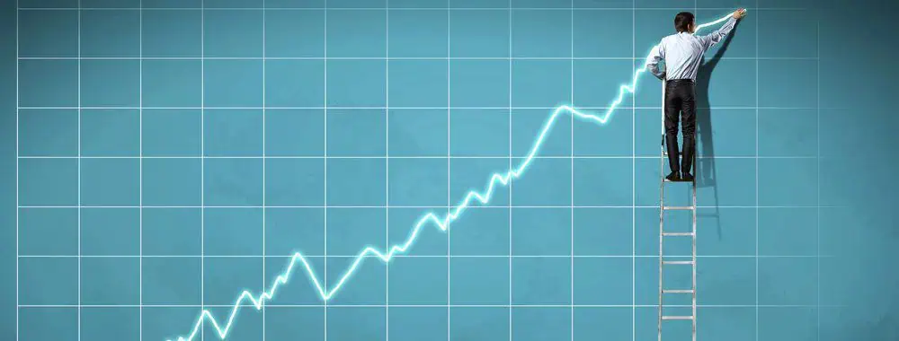 A man on a ladder drawing the line of a graph very high on a wall