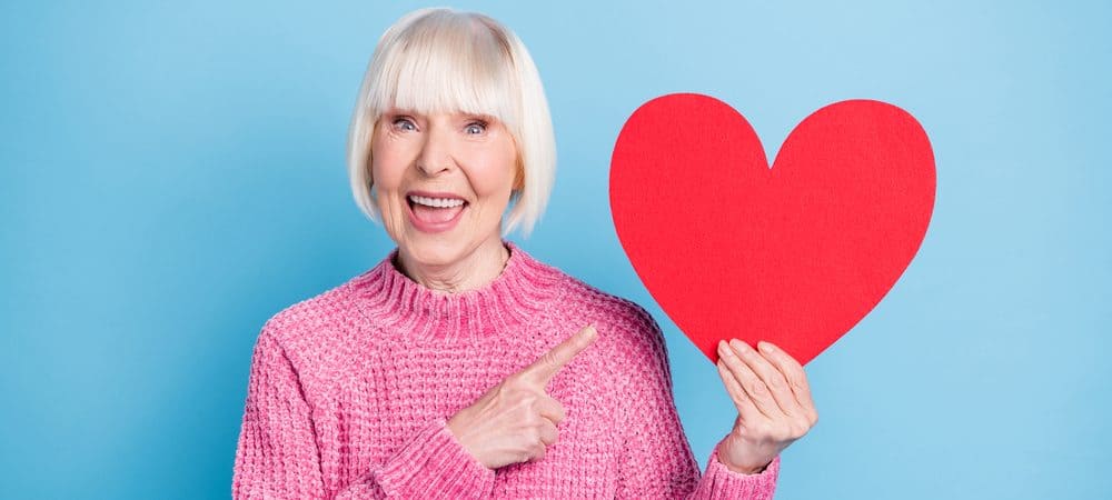 Heart A smiling woman holding up and pointing to a cardboard cut-out of a heart