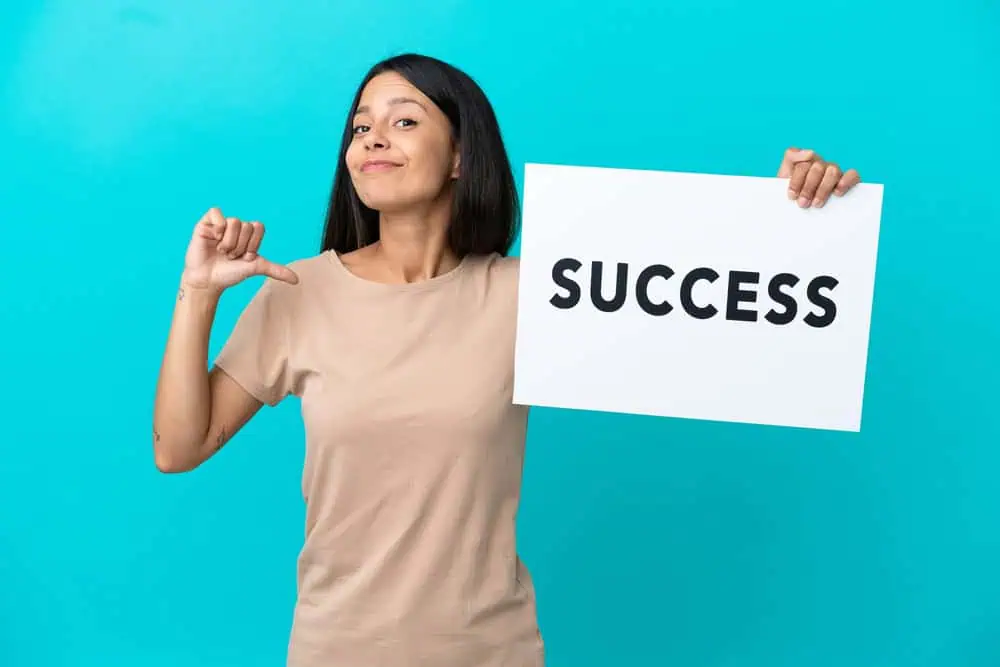 Woman holding pointing to herself while holding a sign that reads "success"