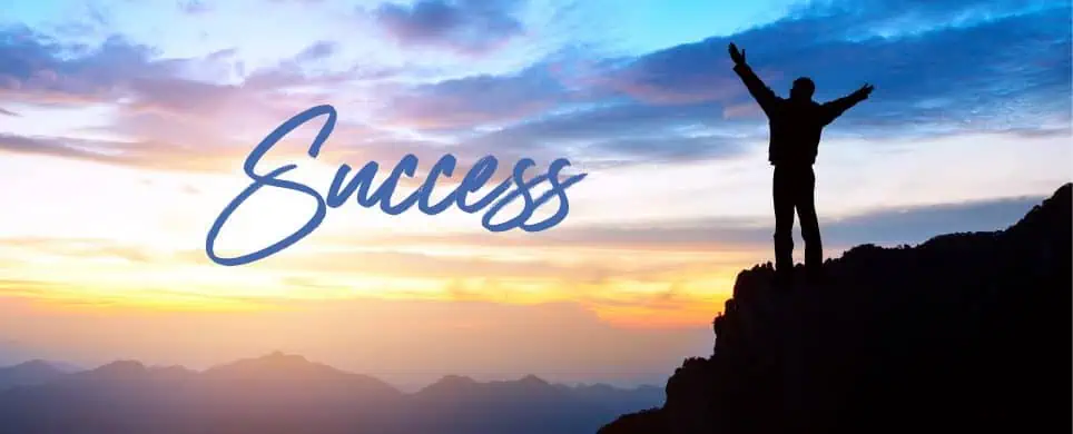 Man standing atop a mountain celebrating success at the break of dawn