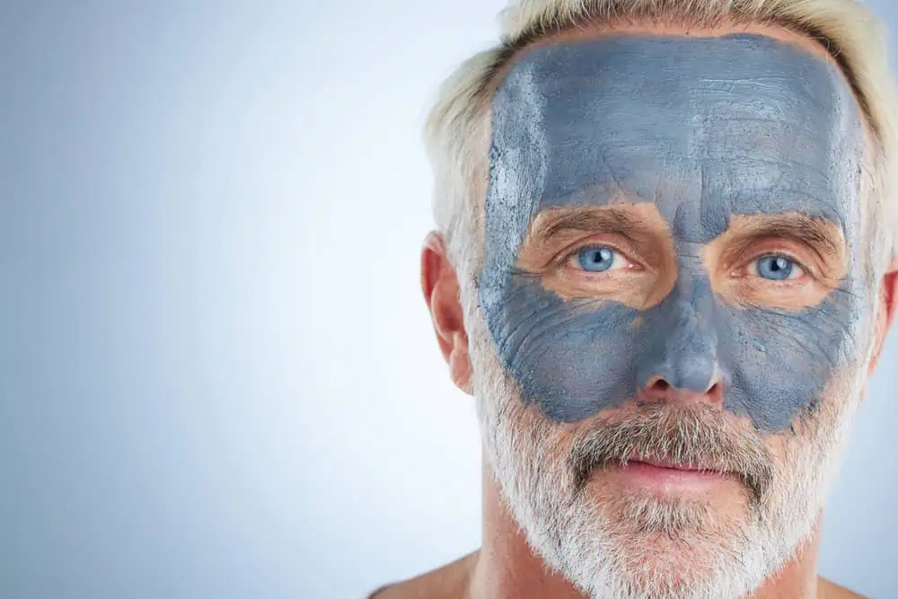 An older man with a mudpack on his face