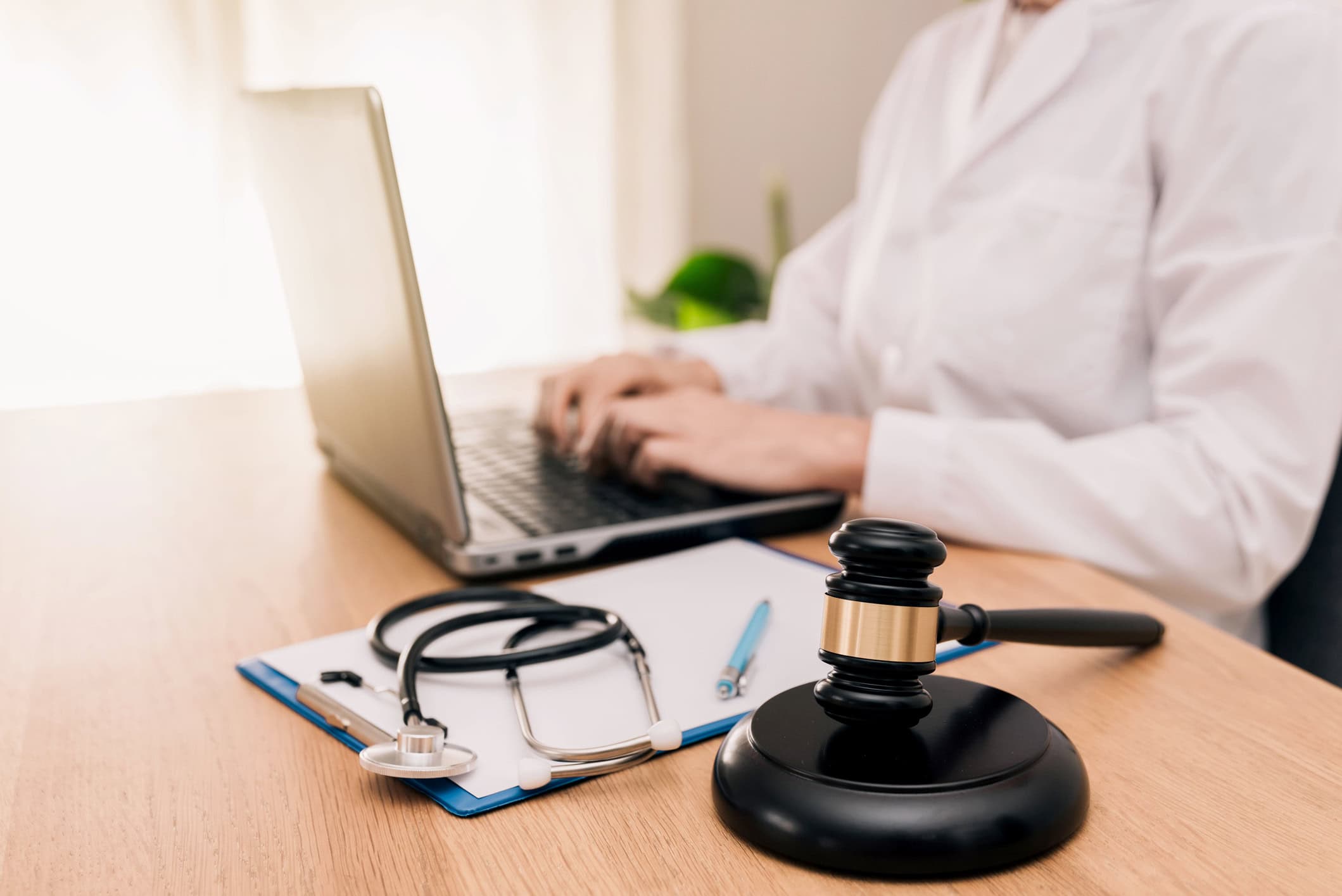 close up of Healthcare Professional Working on Laptop with Gavel, clipboard and Stethoscope on Desk, Medical Law and justice concept