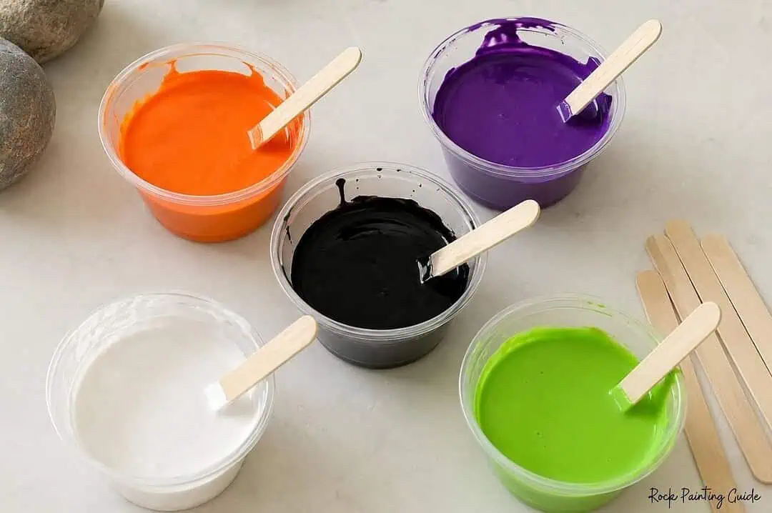 Halloween Paint Pouring on Rocks: Easy Acrylic Pour Tutorial 6 Orange, purple, black, white, and green acrylic paint in cups ready for Halloween paint pourin