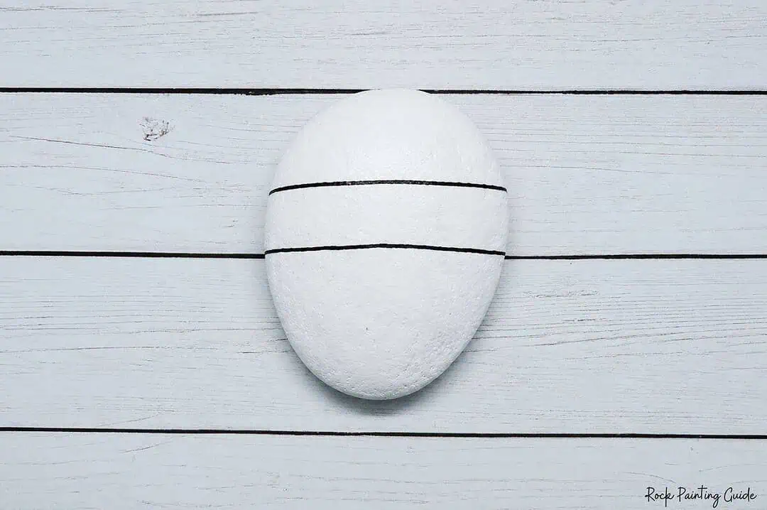 Easy Mummy Rock Painting: Step-by-Step Halloween Tutorial 5 White oval rock with black lines for painting design on wooden background.