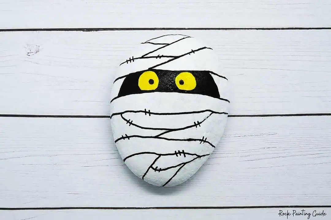 Easy Mummy Rock Painting: Step-by-Step Halloween Tutorial 8 Mummy-themed painted rock with yellow eyes and bandage design.