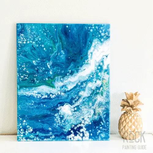 8 Easy Paint Pouring Techniques to Create Beautiful Wall Art 8 flip cup paint pouring technique using blue, white and green with a gold pineapple on a table