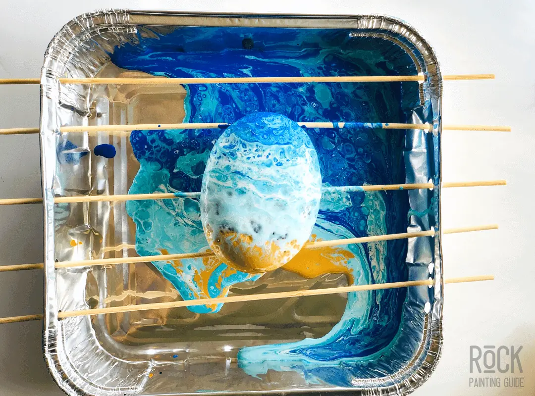 8 Easy Paint Pouring Techniques to Create Beautiful Wall Art 5 paint pouring tray with a paint poured stone on top