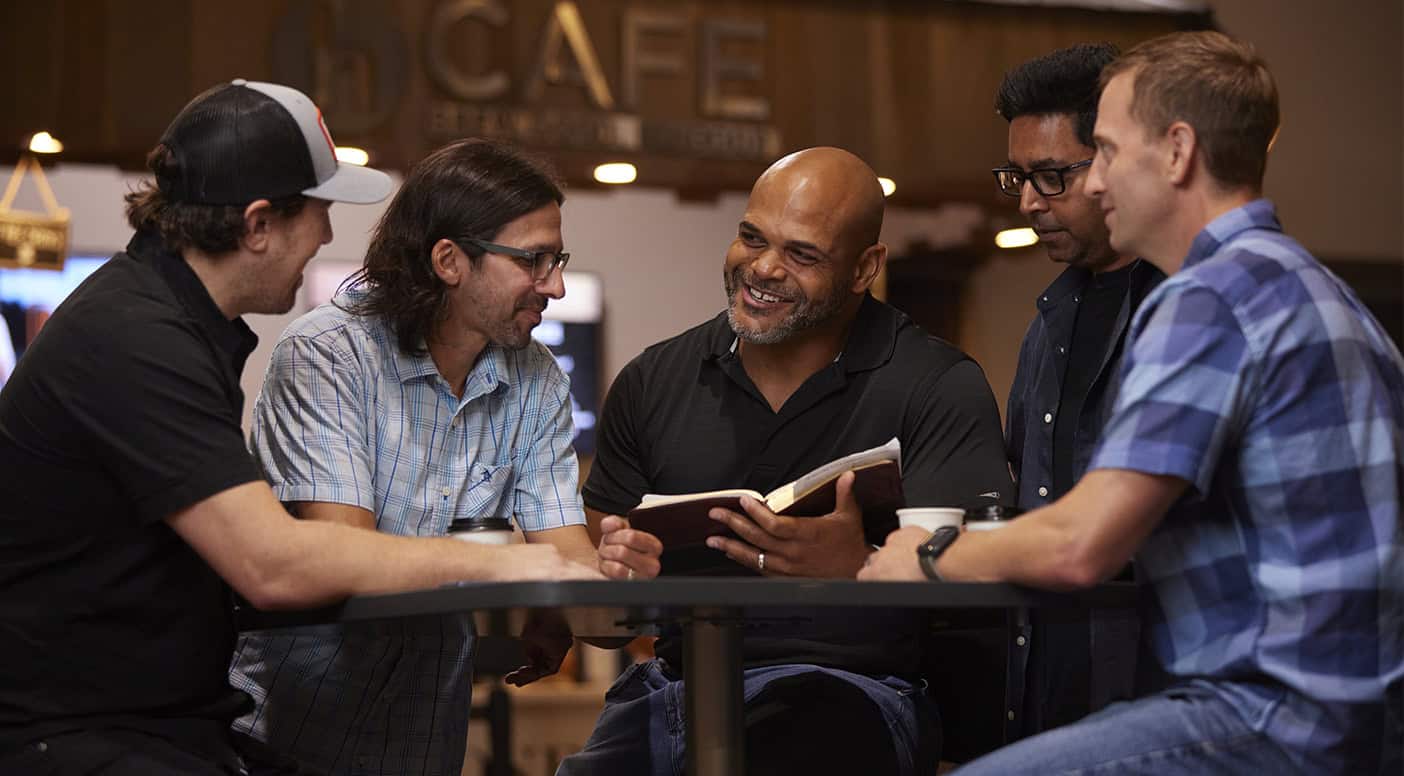 a group of five men talking and reading together
