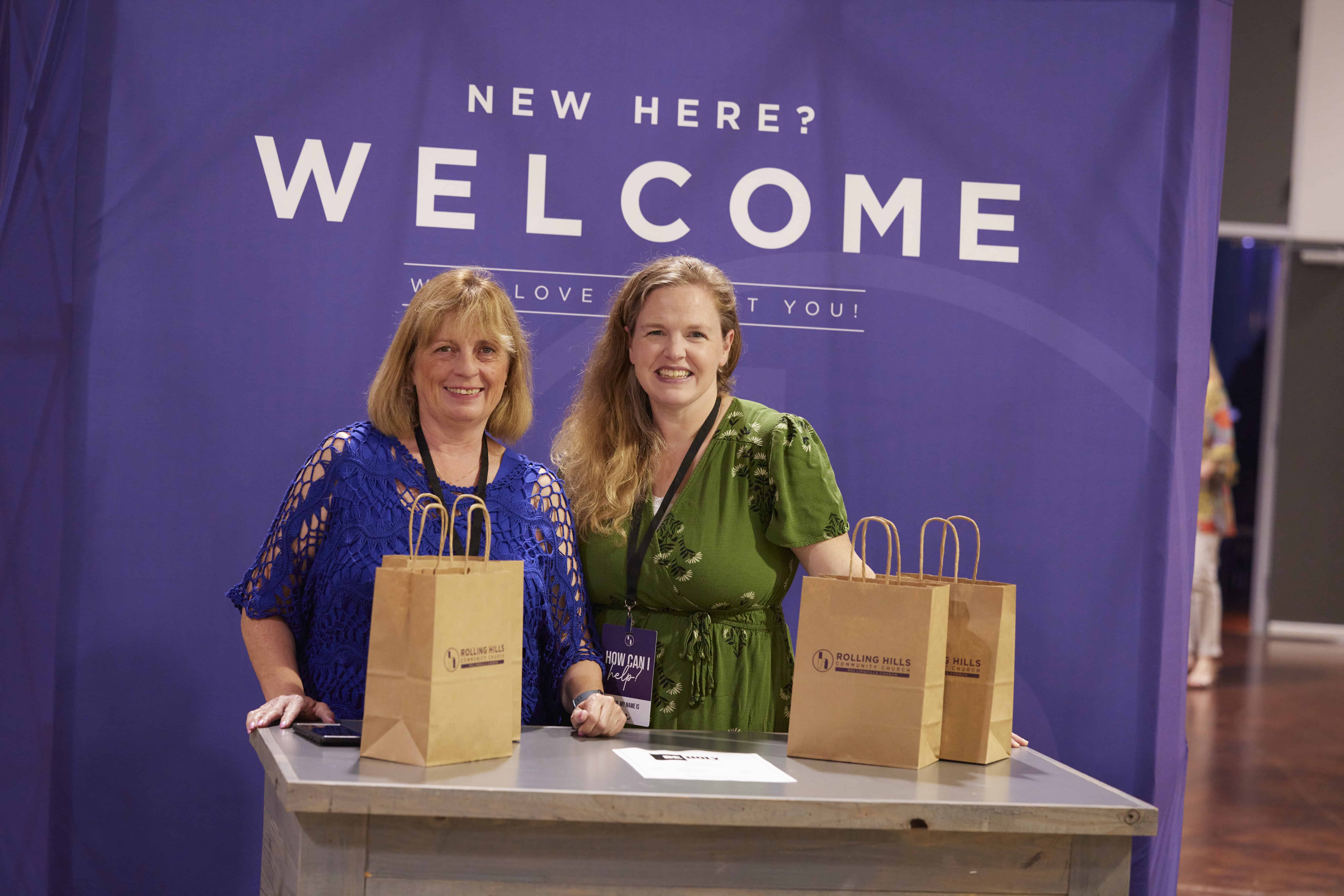 Two women smiling at the welcome desk during church event.