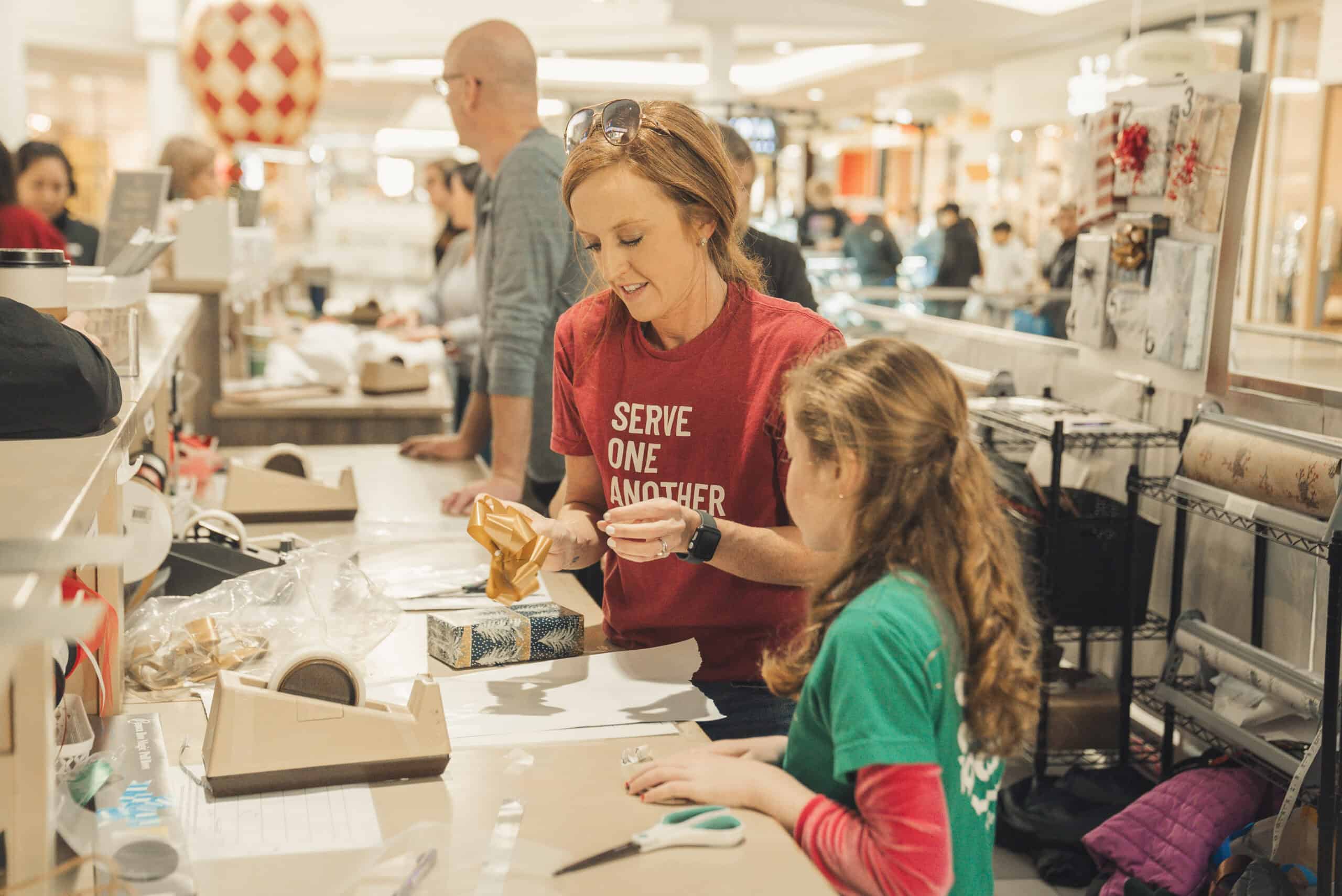 Woman and girl wrapping Christmas gifts at church event, holiday charity activity.