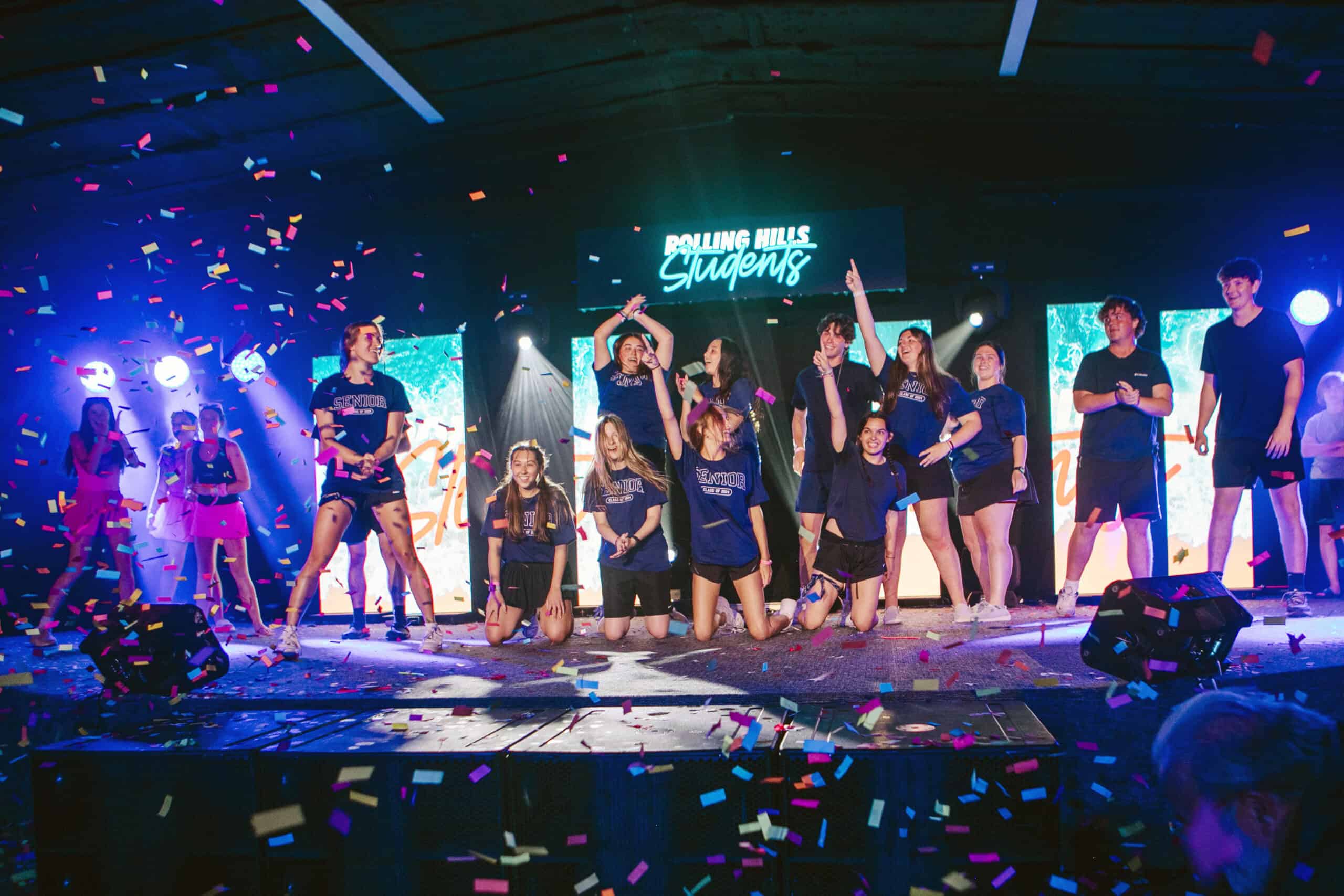 Youth group performing on stage with confetti and vibrant lighting.