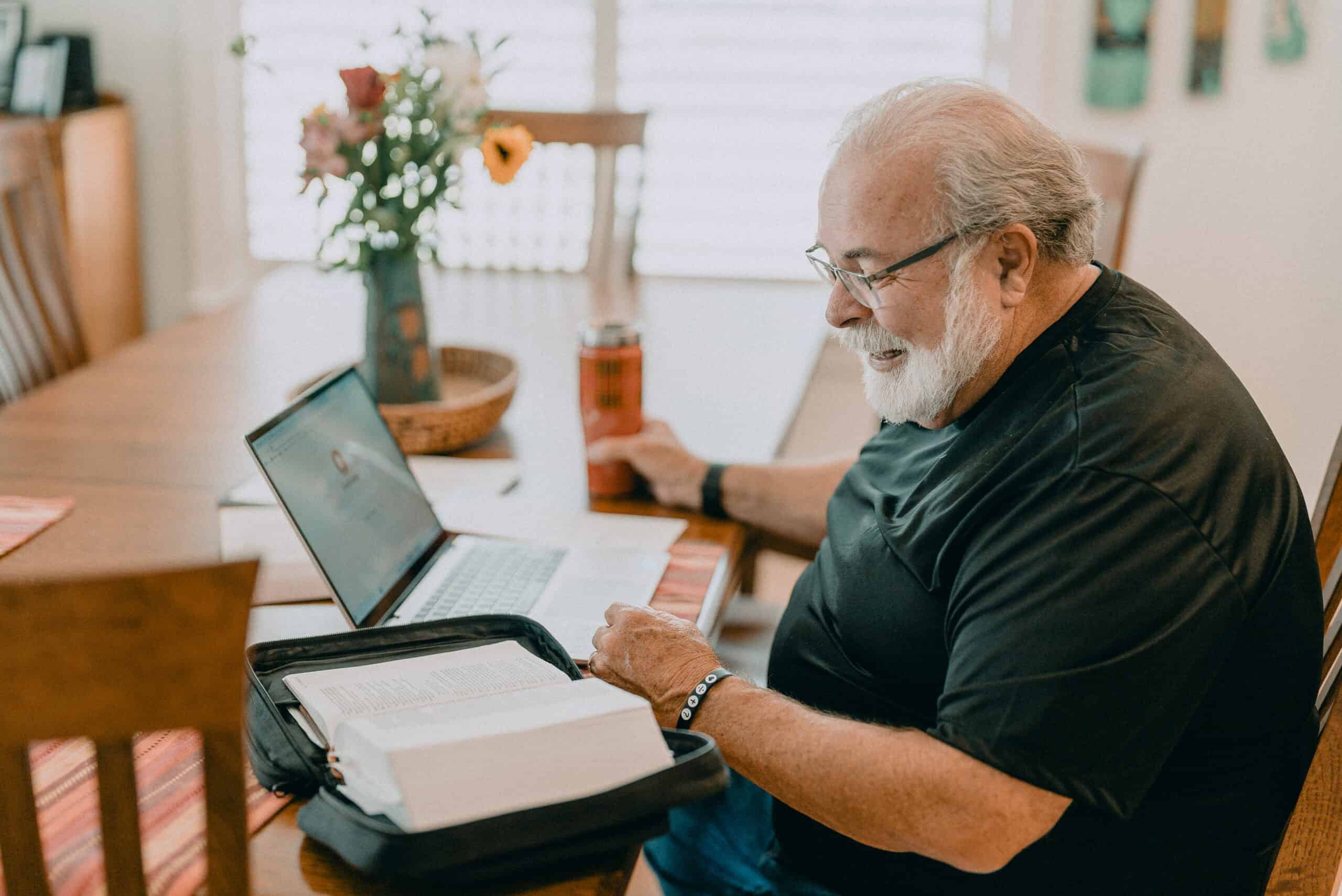 Online church service participation from home with a senior man reading scripture.