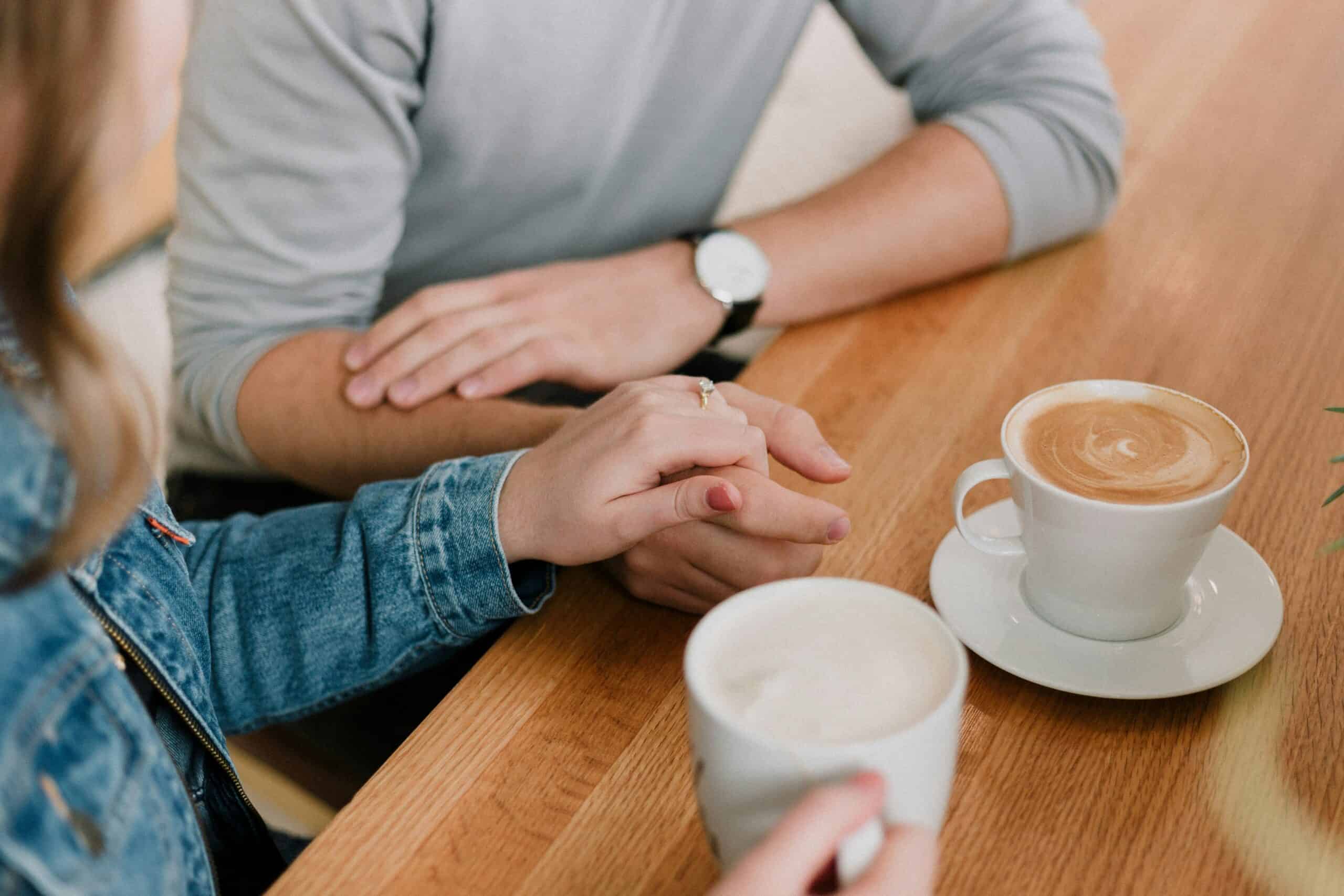 Two people holding hands with coffee cups on a wooden table at Rolling Hills Community Church.