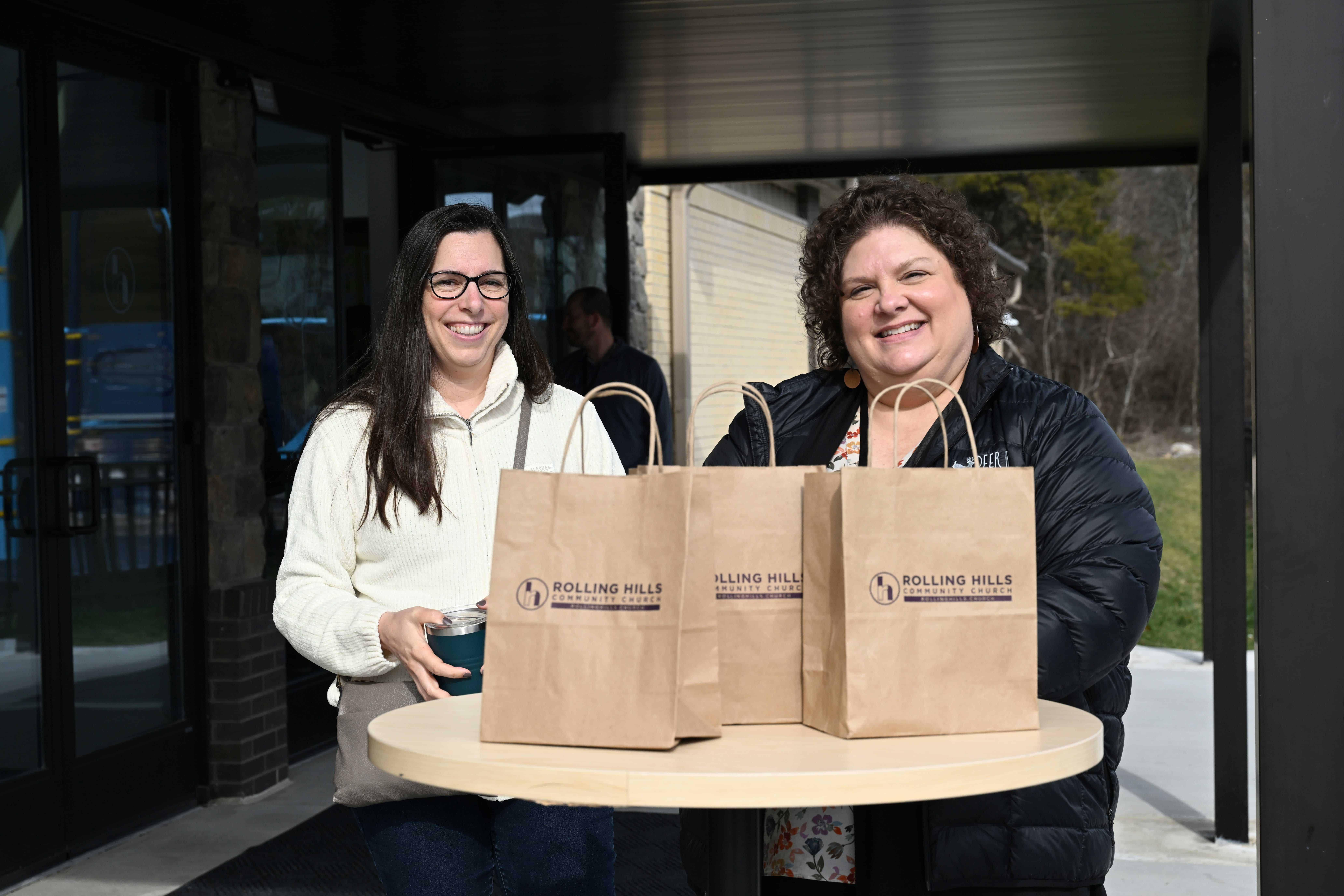 Two women smiling with shopping bags outside Rolling Hills Community Church.