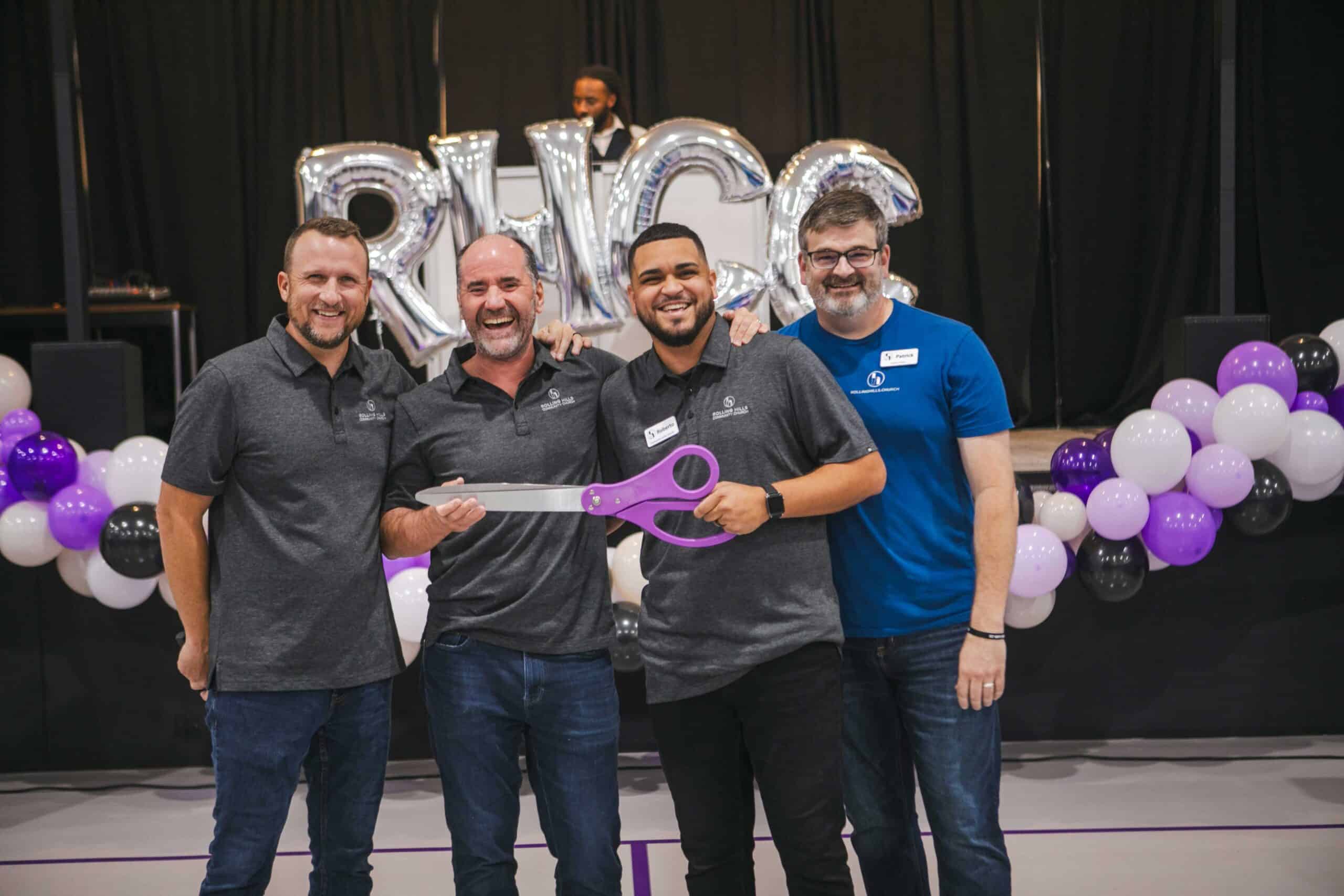 Group of four men celebrating with large scissors at Rolling Hills Church event.