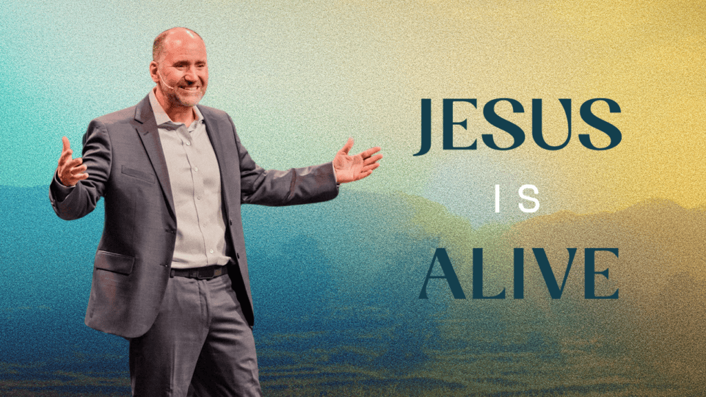 Man in suit with open arms, smiling, with mountains in background, promoting Jesus' resurrection.