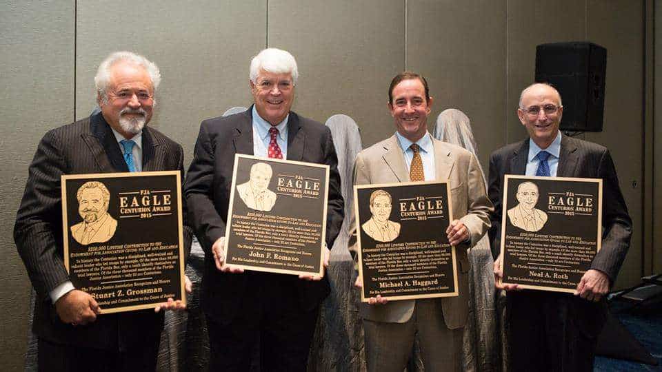 Four men holding Eagle Award plaques at Romano Law Group event in a conference room.